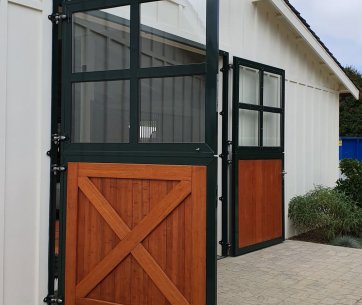 Geöffnete Stalltür der Milberry Farm mit eleganter Holzverkleidung und grüner Stahlkonstruktion