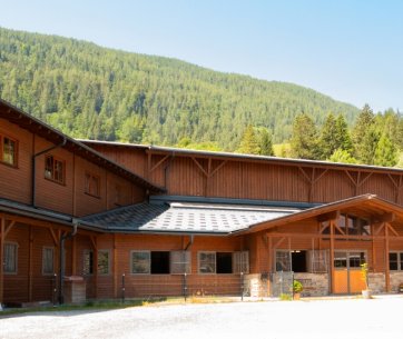 Stallgebäude von Jacpoint Quarterhorses vor bewaldetem Alpenhintergrund bei Sonnenschein