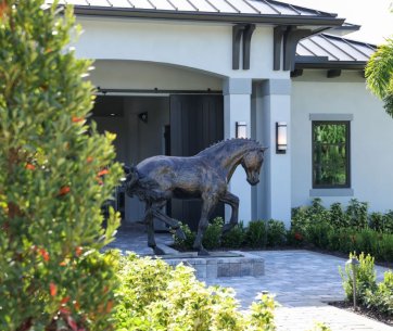 Une statue de cheval en bronze se dresse devant l'entrée élégante de ROasis Riding Oasis, entourée de jardins bien entretenus.