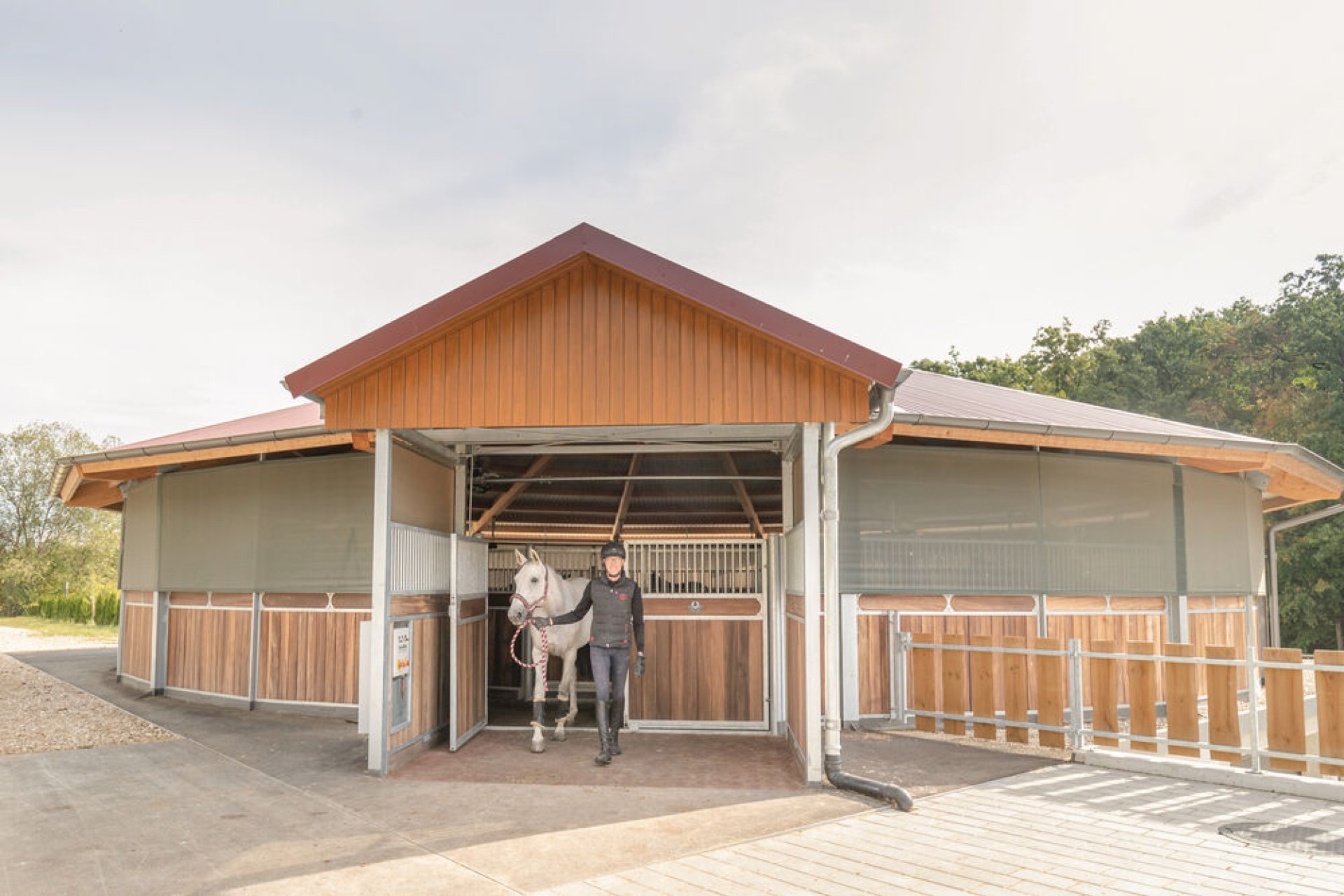 Ein Mann fuehrt sein Pferd aus einer Fuehranlage mit Vordach