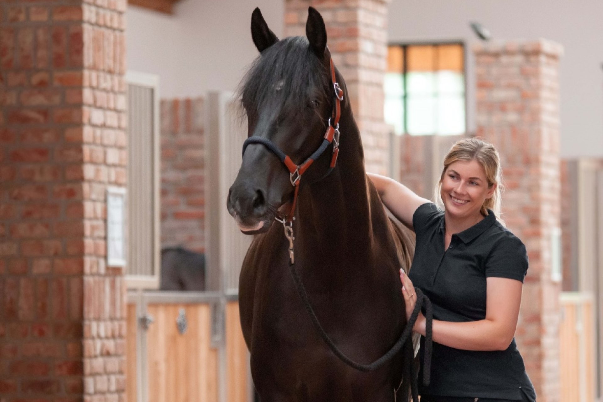 Zufriedene Stallbesitzerin steht vor einer Pferdebox, neben ihrem Pferd und strahlt es an