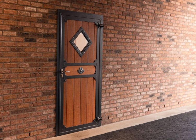 Équipement d’écurie avec une porte d’écurie fermée, remplie de bambou et une fenêtre en losange, intégrée dans un mur en briques.