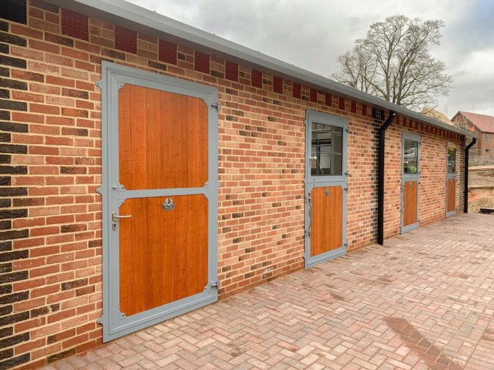 Équipement d’écurie avec une combinaison de portes extérieures galvanisées et de portes d’écurie en bois massif dans une façade en briques rouges.