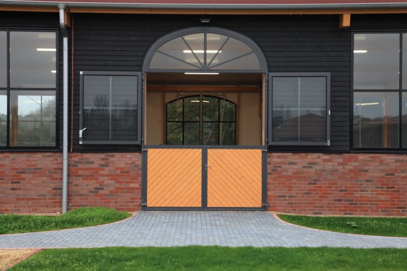 Équipement d’écurie avec porte à quatre battants et arc décoratif en forme de soleil, intégré dans une façade moderne en briques et bois.